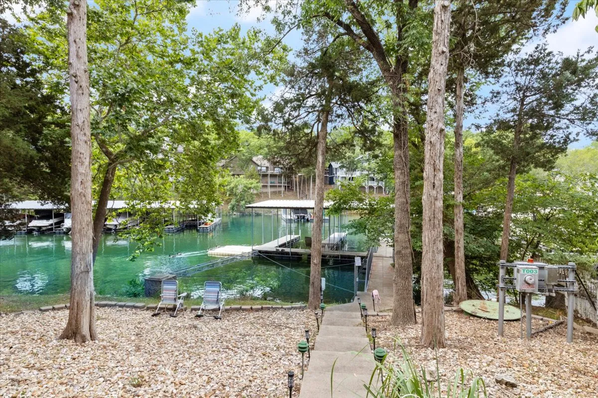 A lakeside view featuring docks, lounge chairs, and trees, offering a serene and welcoming spot for both water activities and relaxation by the shore. The arrangement suggests a seamless transition from home to lake, with ample space for gathering or preparing for an adventure.
