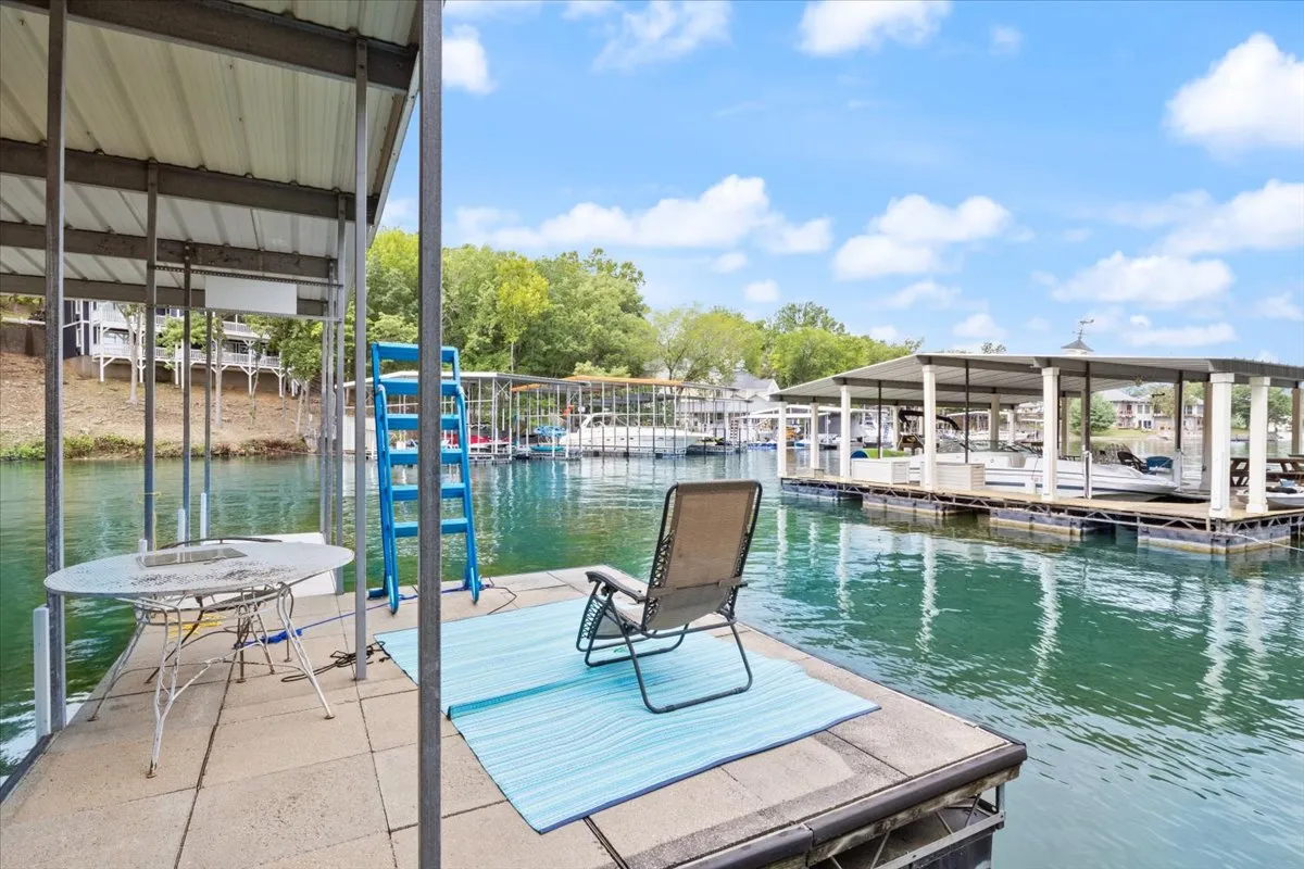 A closer perspective of a dock with a lounge chair and table, surrounded by lush greenery and calm water. The setting invites relaxation, sunbathing, and leisure, with easy access to the water for swimming, fishing, or launching watercraft.