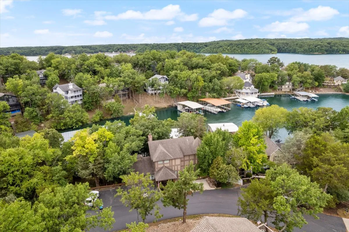 A tranquil view of the lakefront property with a dock extending into the shimmering water, surrounded by trees and nearby homes. The scene hints at boating opportunities and peaceful relaxation by the water.