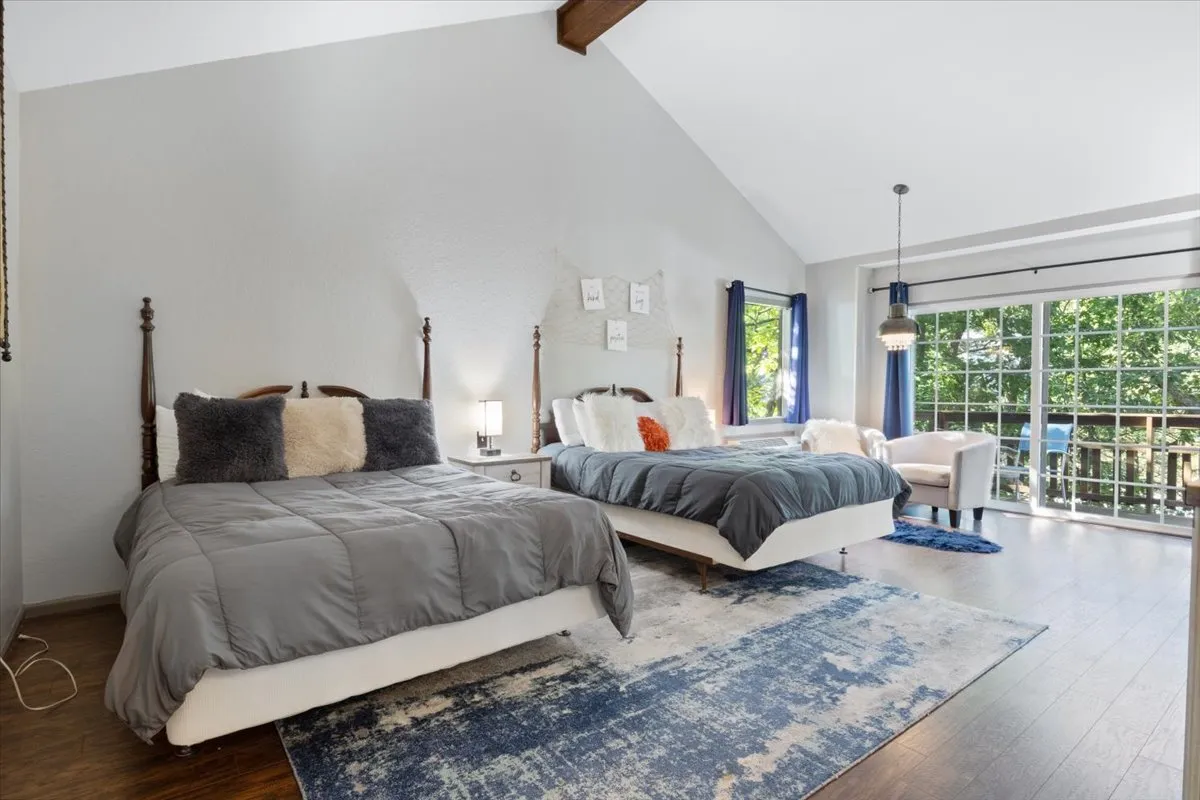 A spacious bedroom featuring two beds, a cozy seating area by large windows, a decorative rug, and abundant natural light. The layout allows for both socializing and privacy, with inviting spaces to read or enjoy breakfast in bed.