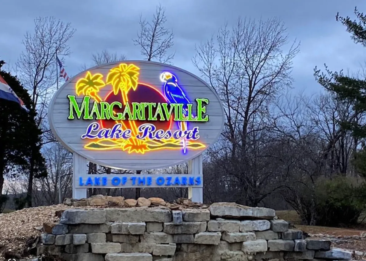 This exterior image showcases the vibrant Margaritaville sign illuminated by colorful neon lights, with a stone base and hints of the lakeside resort ambiance. The scene suggests a lively, fun, and inviting atmosphere perfect for lakeside entertainment, dining, and nightlife. It visually references the lakeside eateries and entertainment options discussed in the section.