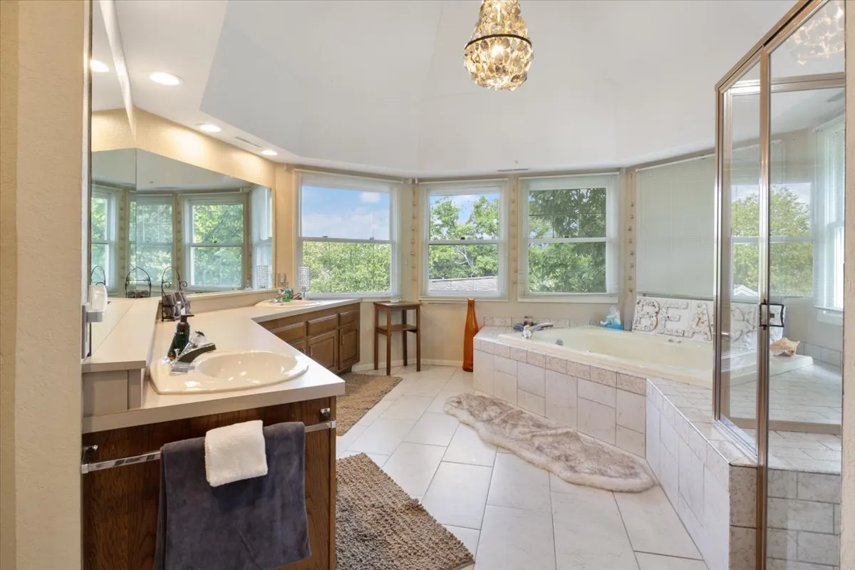A modern bathroom with a luxurious bathtub positioned by large windows, a vanity area, and an elegant chandelier overhead. The setting is serene and spacious, with natural light highlighting the opportunities for relaxation and self-care.