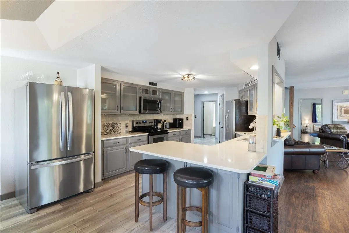 A contemporary kitchen scene featuring a large stainless steel refrigerator, quartz countertops, bar stools at the counter, and well-organized cabinets. The space is designed for socializing and cooking, with a welcoming, modern aesthetic.