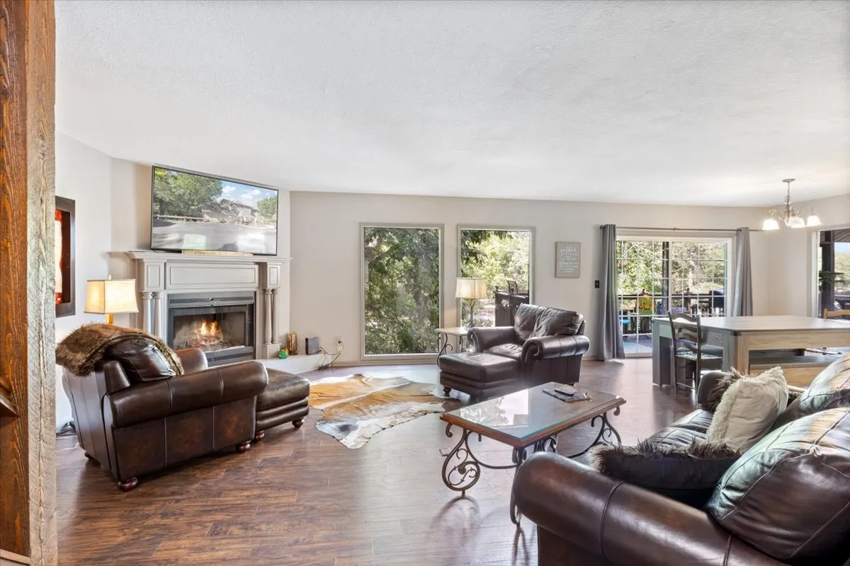 A spacious open-concept area featuring a large dining table adjacent to a cozy seating area with a fireplace and expansive windows. The room is filled with natural light, creating a warm and welcoming environment ideal for gatherings and family activities.