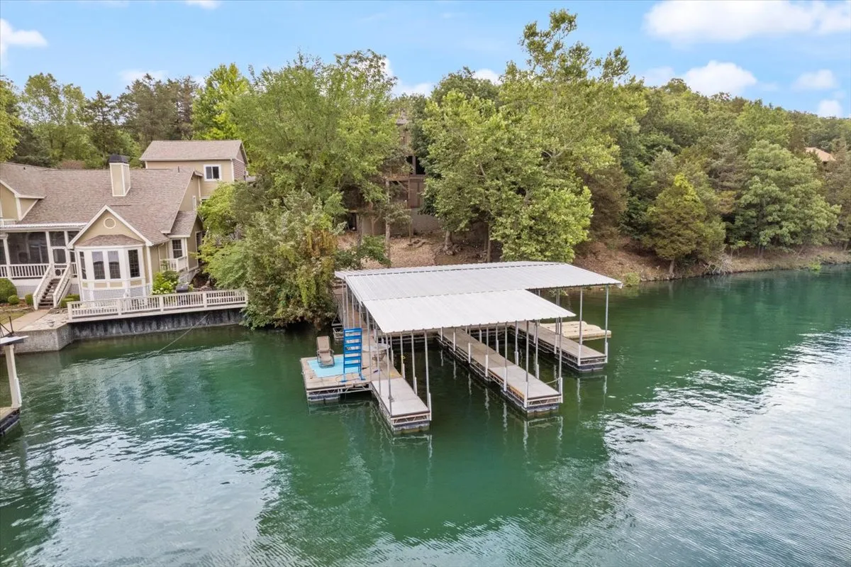 A scenic lakefront scene featuring a private dock stretching over the water, with the house and lush surrounding trees visible in the background. The dock is built for both relaxing and launching watercraft, capturing the essence of lakefront living.